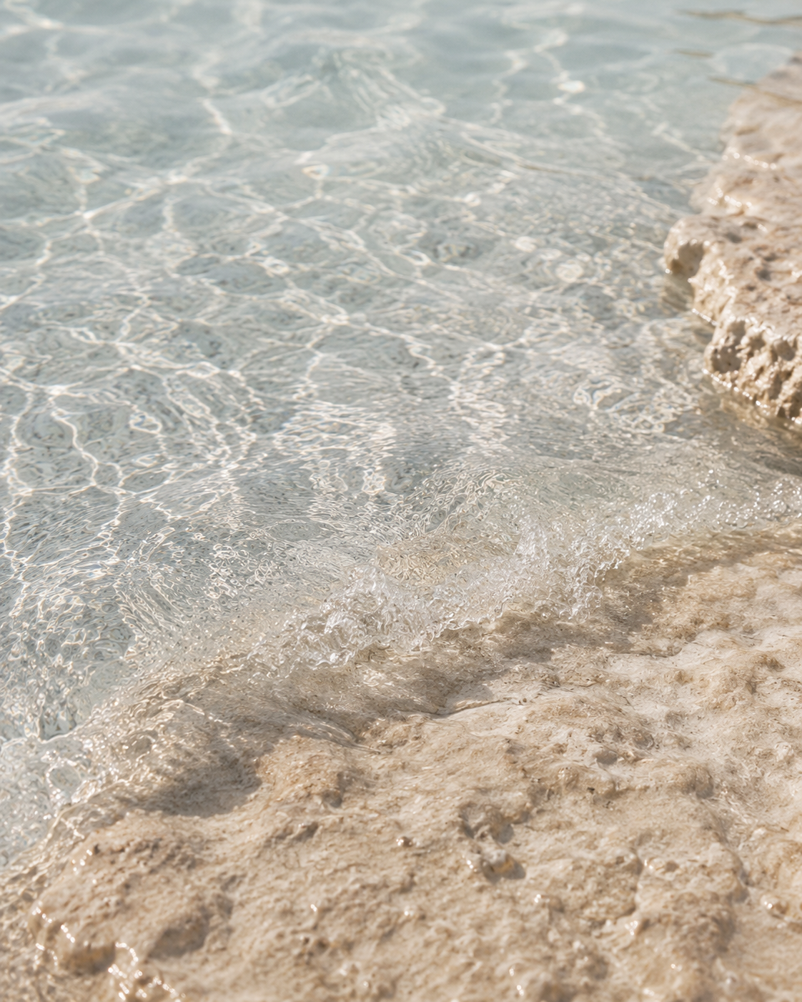 Pale, clear ocean water meeting soft, sunlit mineral stone.